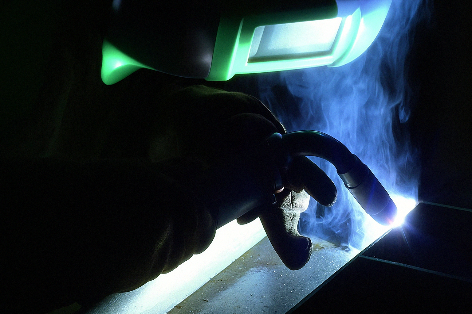 Hand wearing a welding helmet with a glowing light source, likely from welding activity.